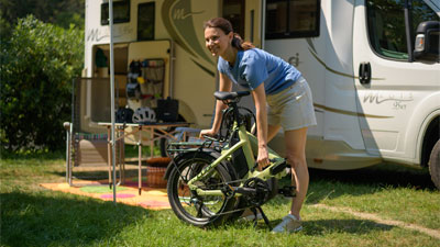 Una donna è in piedi davanti a un camper, davanti a lei c'è una bicicletta pieghevole verde.