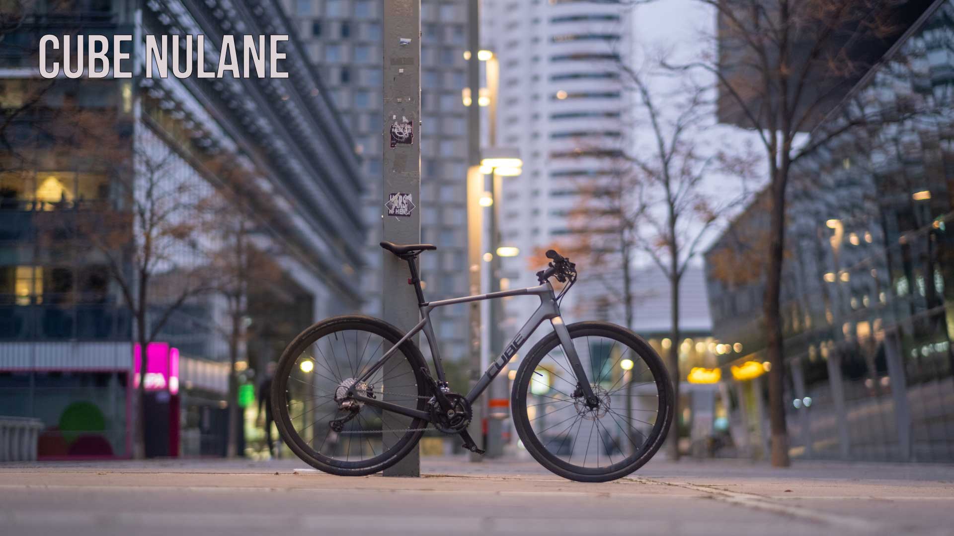 Striscione con la scritta Cube Nulane. Una cyclette Cube Nulane è appoggiata a un pilastro nel centro della città.