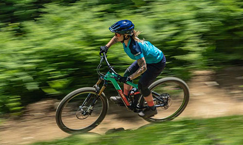 Si vede una donna su una mountain bike che corre veloce su un sentiero nel bosco. 