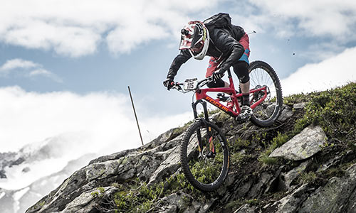 Ciclista downhill con casco integrale che scende su rocce lungo un pendio montuoso.