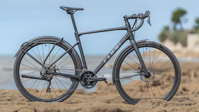Si vede una bicicletta Cube Gravel nera, in piedi su un terreno roccioso, con la costa sullo sfondo.