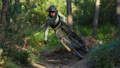 Ciclista che attraversa il bosco in diagonale su una mountain bike Cube Stereo Fully.
