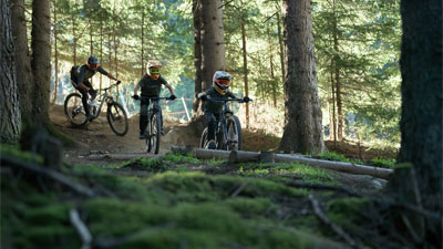 Due adolescenti e un ciclista attraversano il bosco su mountain bike Cube Stereo Fully.