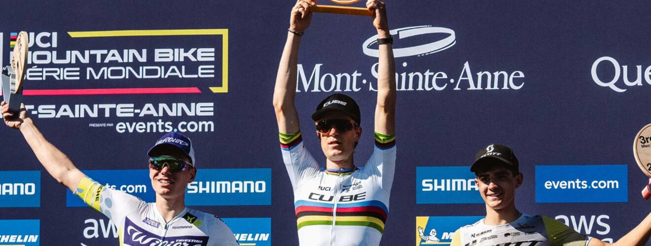 Finn Treudler festeggia alla finale di stagione del Cube Factory Racing 2025 a Mont-Sainte-Anne, tenendo il trofeo tra le mani, affiancato dai ciclisti arrivati al secondo e al terzo posto sul podio.